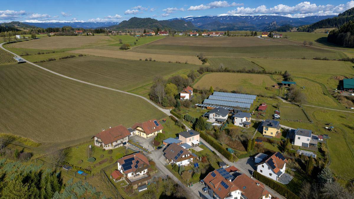 Weitläufige Luftaufnahme einer ländlichen Siedlung mit Feldern und Häusern unter blauem Himmel.