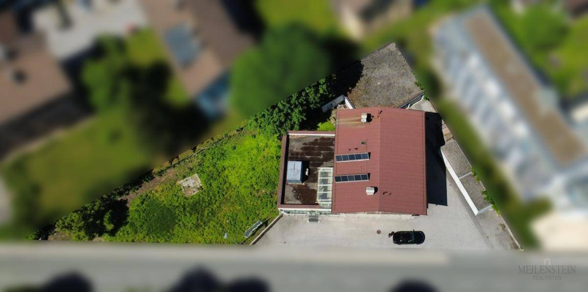 Luftaufnahme eines modernen Gebäudes mit rotem Satteldach, Flachdach und Solaranlage.