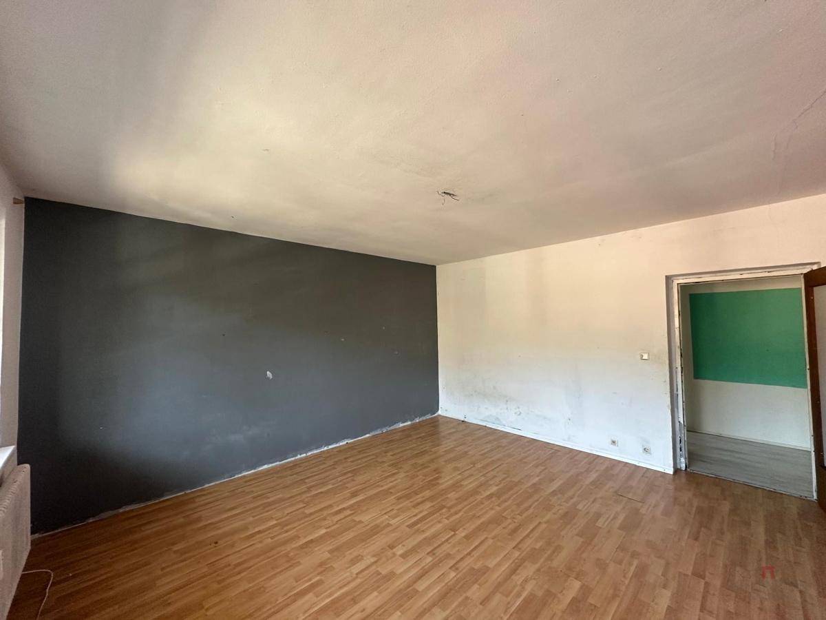 Leeres Zimmer mit Holzboden und einer dunkelgrauen Akzentwand, das eine Renovierung benötigt.
