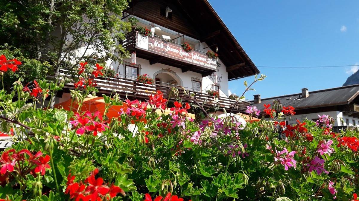 Traditionelles Gasthaus in den Bergen, umgeben von bunten Blumen und grüner Natur.