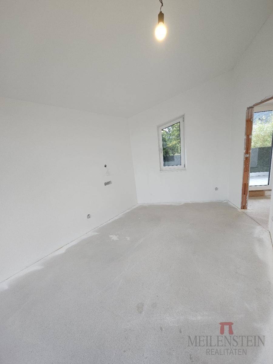 Unfertiges Zimmer mit einem Fenster und Rohbetonboden, bereit für den Ausbau.