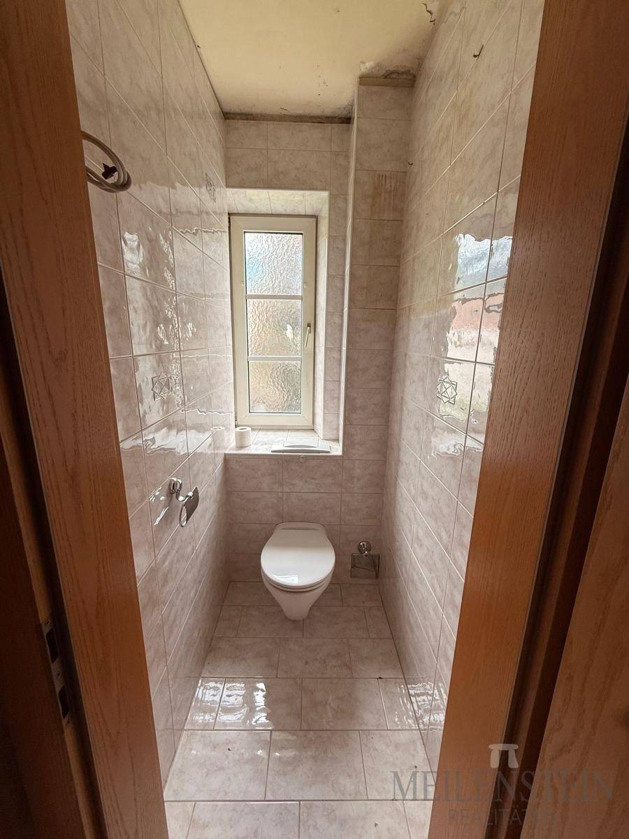 Kleines WC mit Toilette, gefliesten Wänden und Fenster, das eine Auffrischung benötigt.