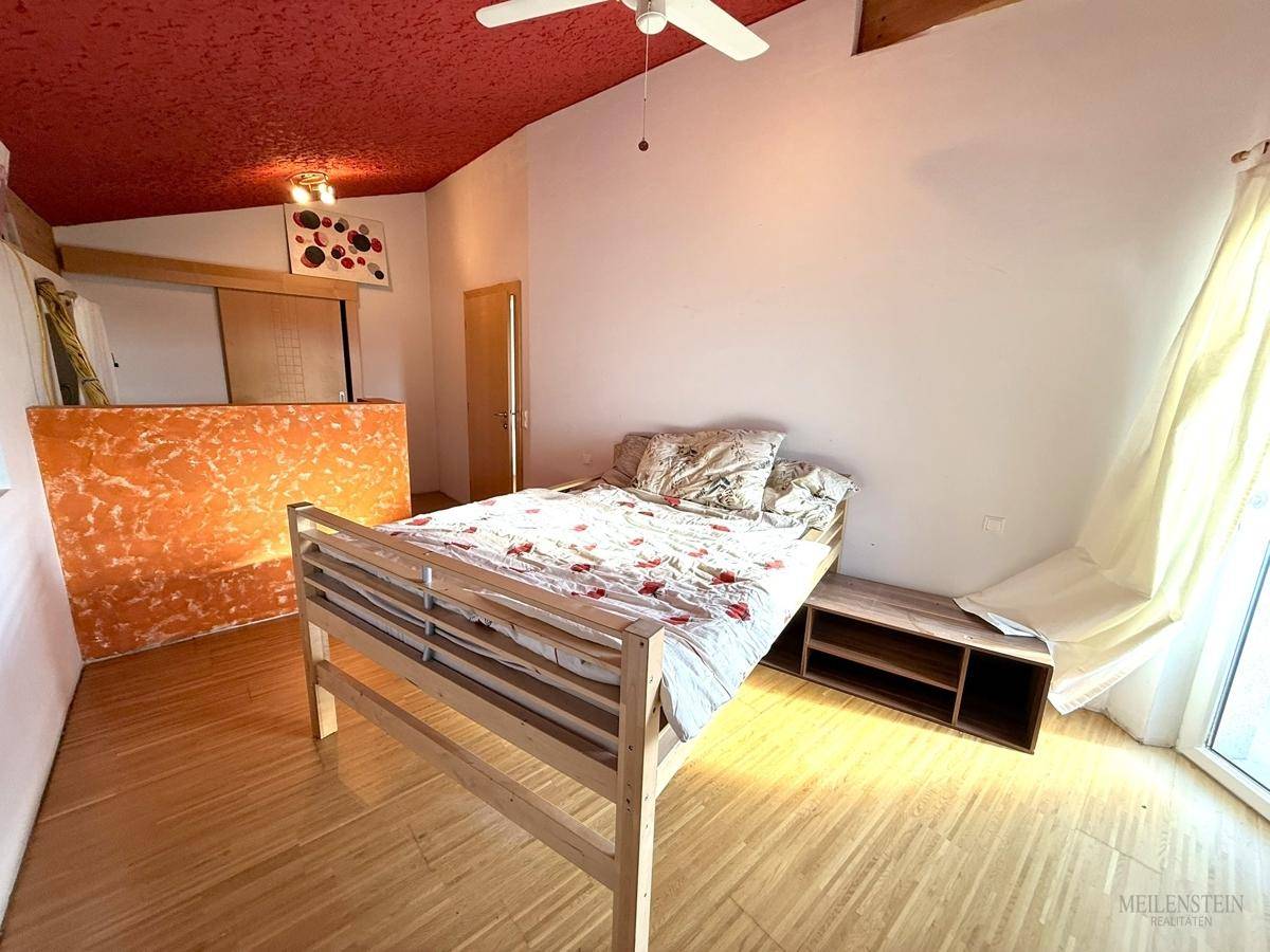 Schlafzimmer mit Holzboden, roter Decke und Zugang zu einem Balkon, hell und geräumig.