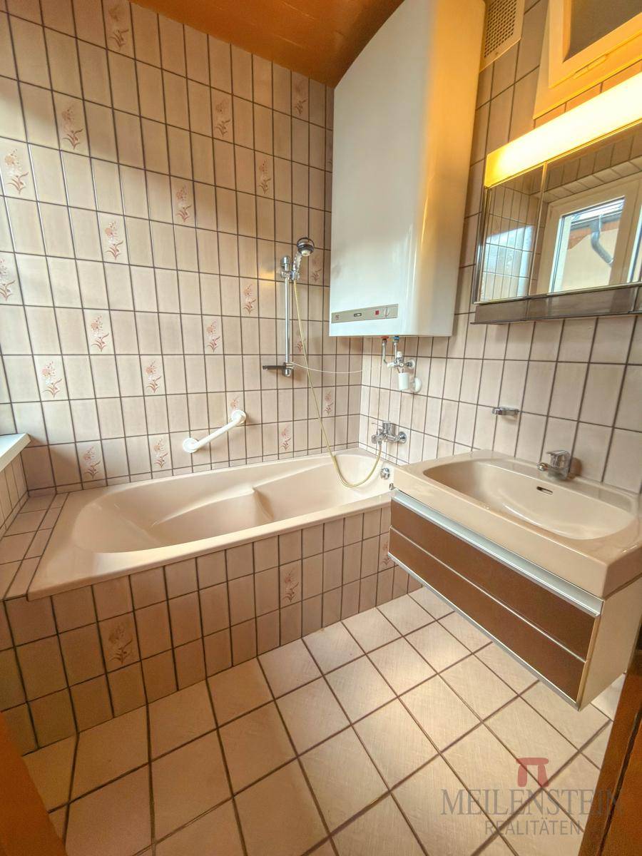 Badezimmer mit Badewanne, Waschbecken und Fliesen im 80er-Jahre-Stil.