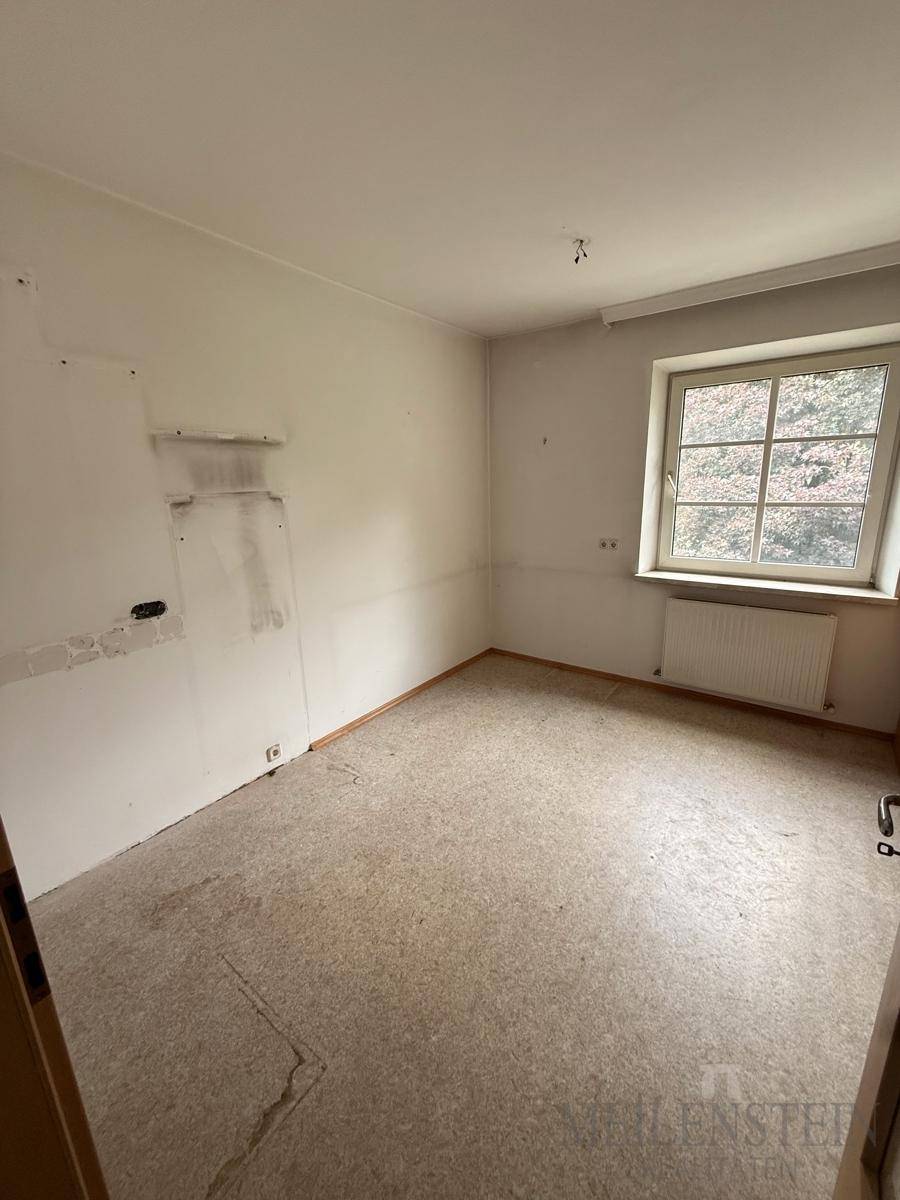 Leeres Zimmer mit Fenster und Heizkörper, bereit für eine Renovierung und neue Bodengestaltung.