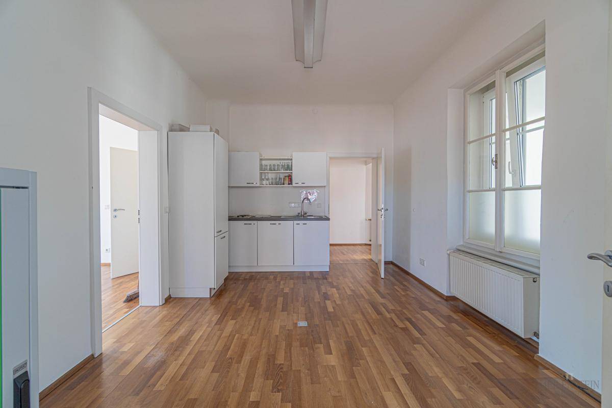 Leerer Raum mit Holzboden und einer kleinen Küchenzeile, ideal für ein Büro oder Arbeitszimmer.