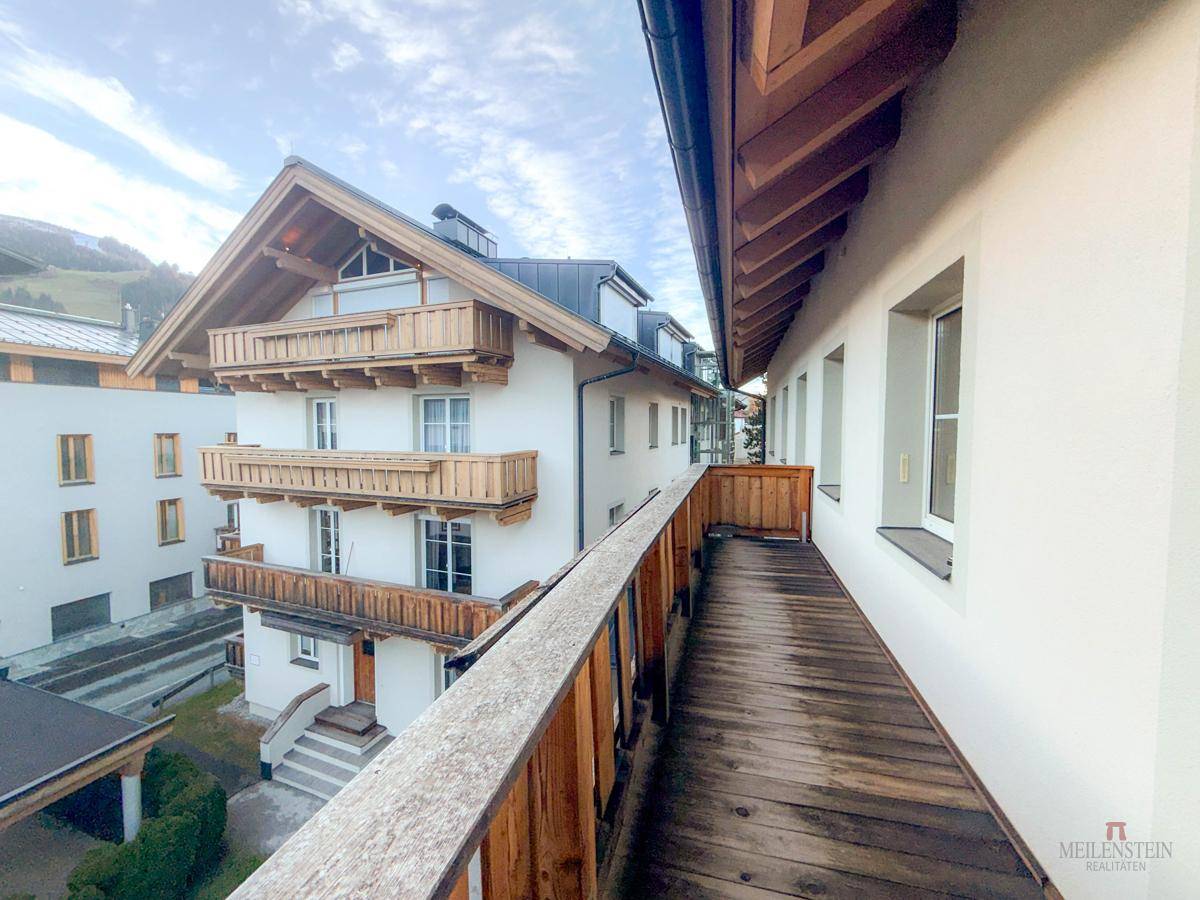 Langer Holzbalkon mit Blick auf die umliegende Berglandschaft und ein traditionelles Gebäude.