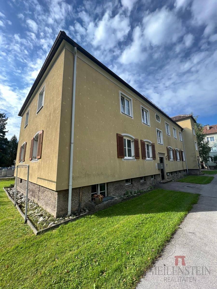 Seitenansicht des Gebäudes mit gelber Fassade, braunen Fensterläden und einem grünen Rasenstreifen.
