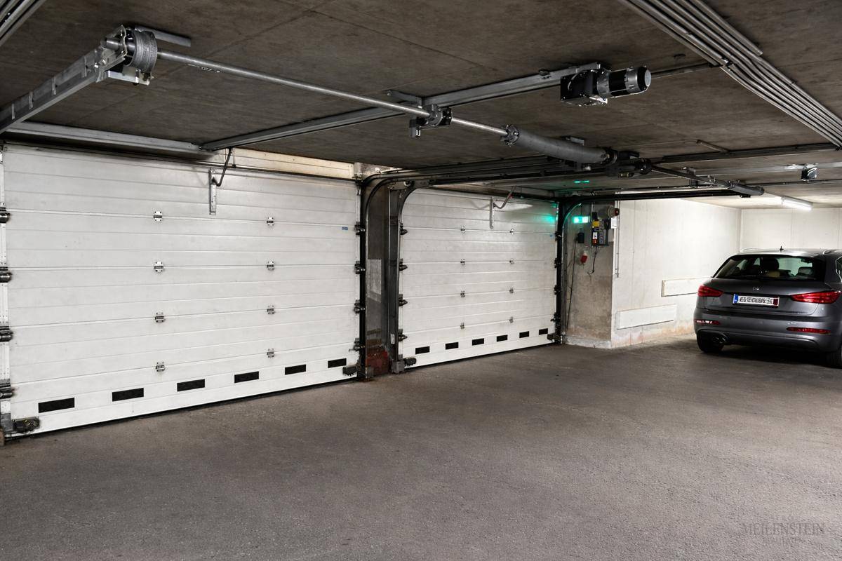 Zwei weiße Garagentore in einer Tiefgarage mit einem geparkten Auto und sichtbaren Deckeninstallationen.