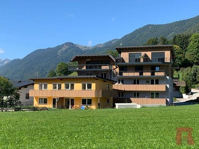 Mehrere moderne Gebäude mit Holzfassaden und Balkonen, eingebettet in eine grüne Berglandschaft.