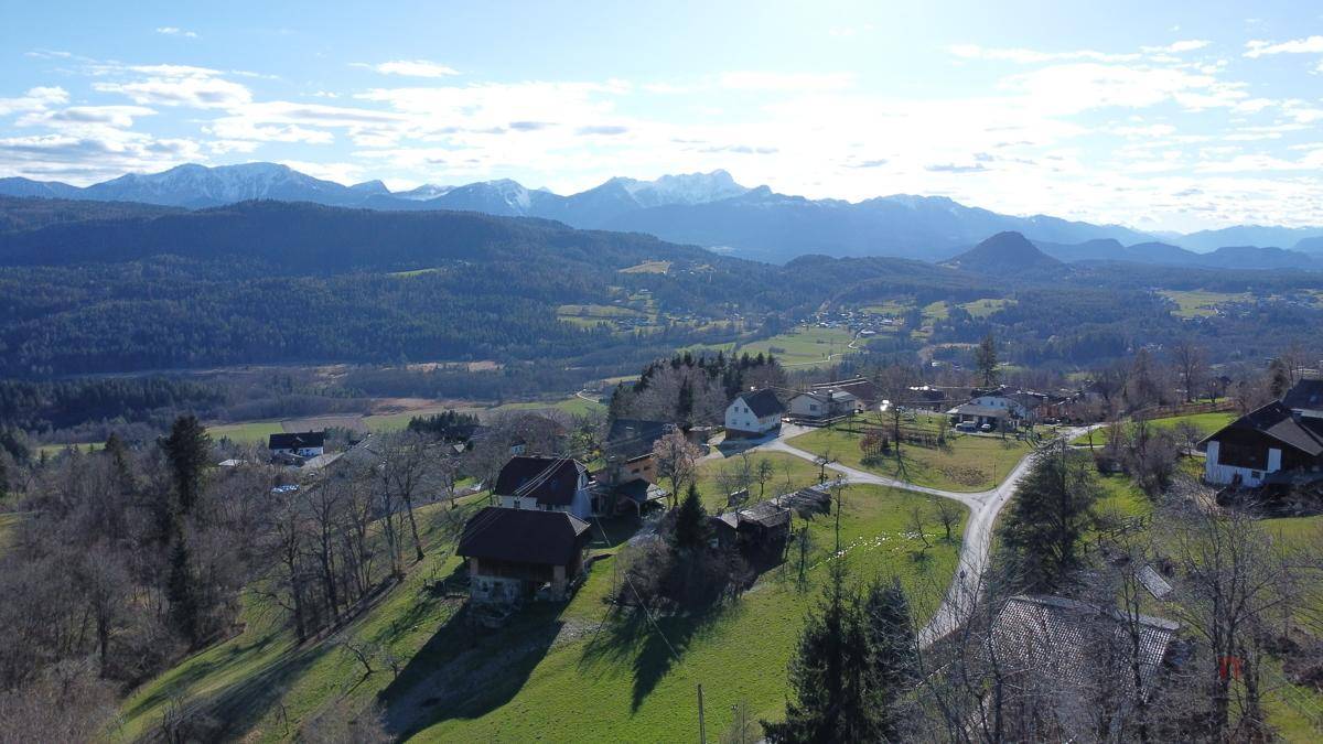 Weitläufige Landschaftsaufnahme mit verstreuten Häusern, grünen Feldern und Bergen am Horizont.