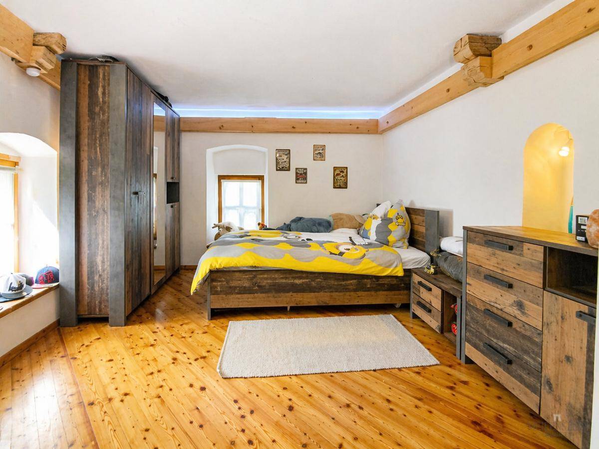 Gemütliches Schlafzimmer mit Holzdielenboden, Holzbalken und rustikalen Möbeln.