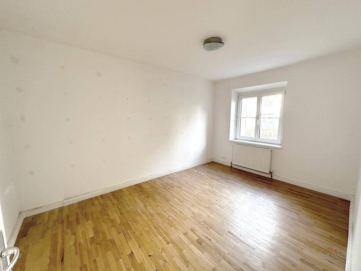 Schlafzimmer mit Parkettboden und Fenster, das viel natürliches Licht in den Raum lässt.