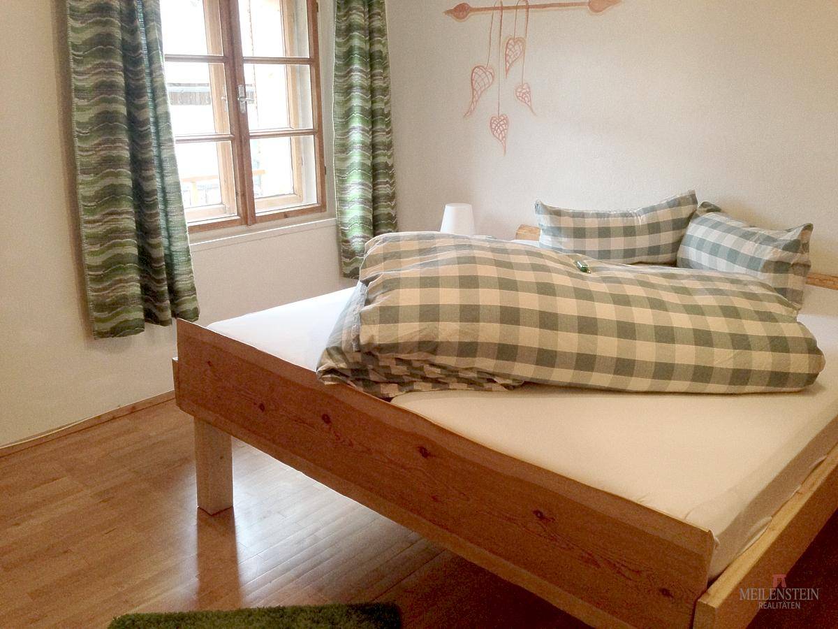 Freundliches Schlafzimmer mit Holzbett, karierter Bettwäsche und Fenster mit grünen Vorhängen.
