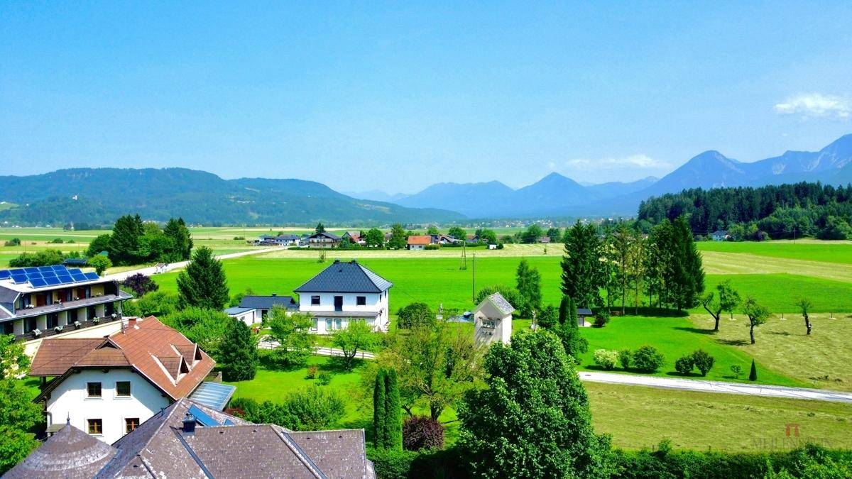 Weitläufiger Blick über die grüne Landschaft mit Bergen und vereinzelten Häusern.