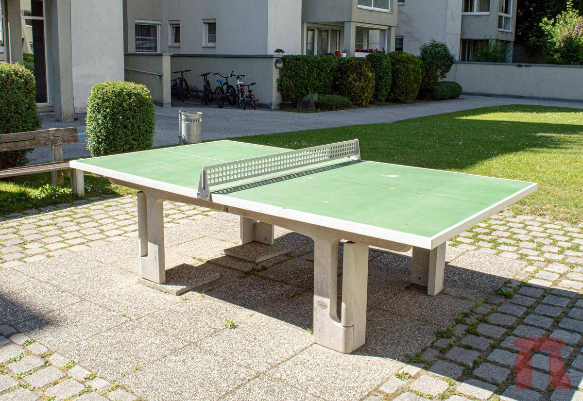 Outdoor-Tischtennisplatte auf einem gepflasterten Bereich im Gemeinschaftsgarten der Anlage.