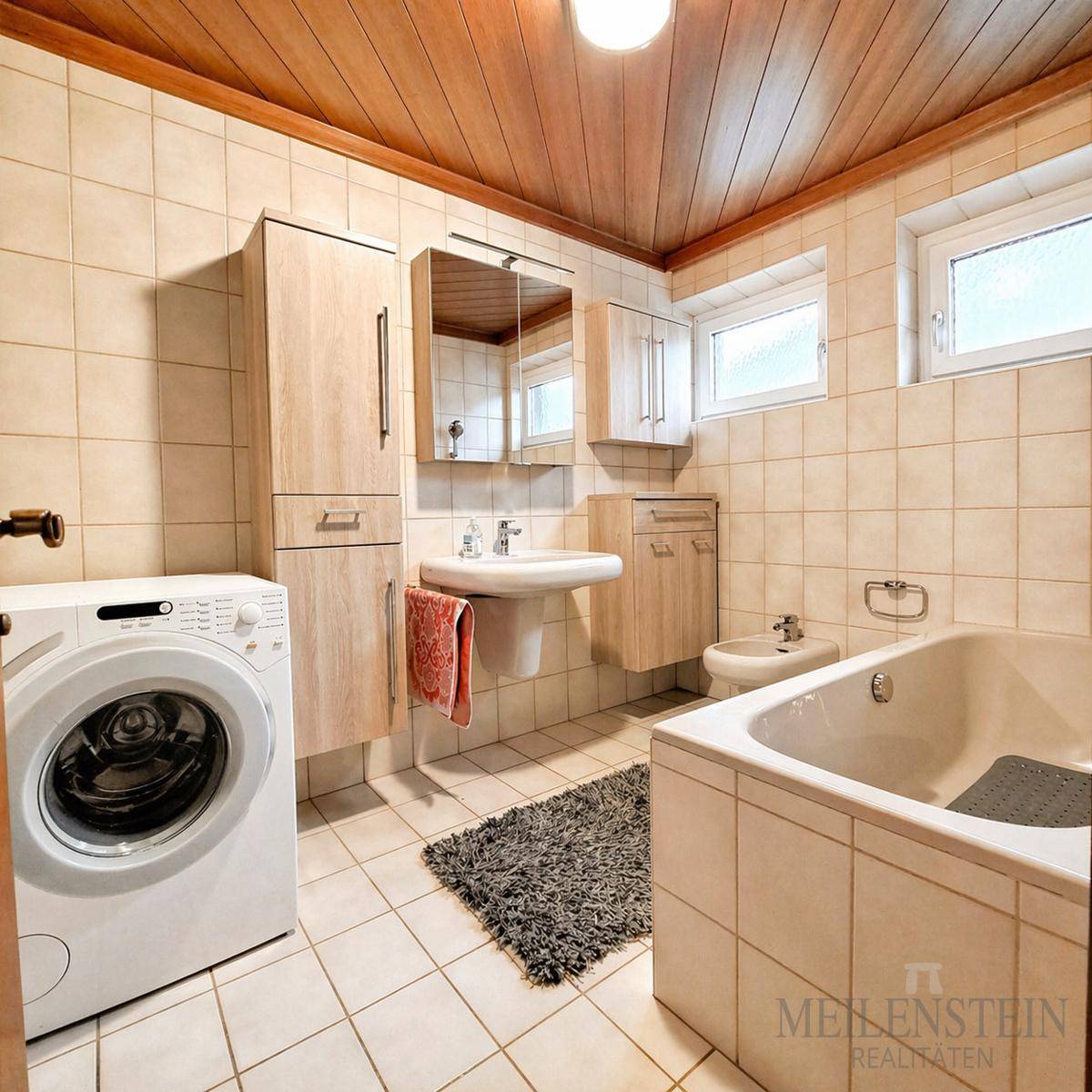 Gefliestes Badezimmer mit Badewanne, Waschbecken, Bidet und einer Waschmaschine, gut gepflegt.