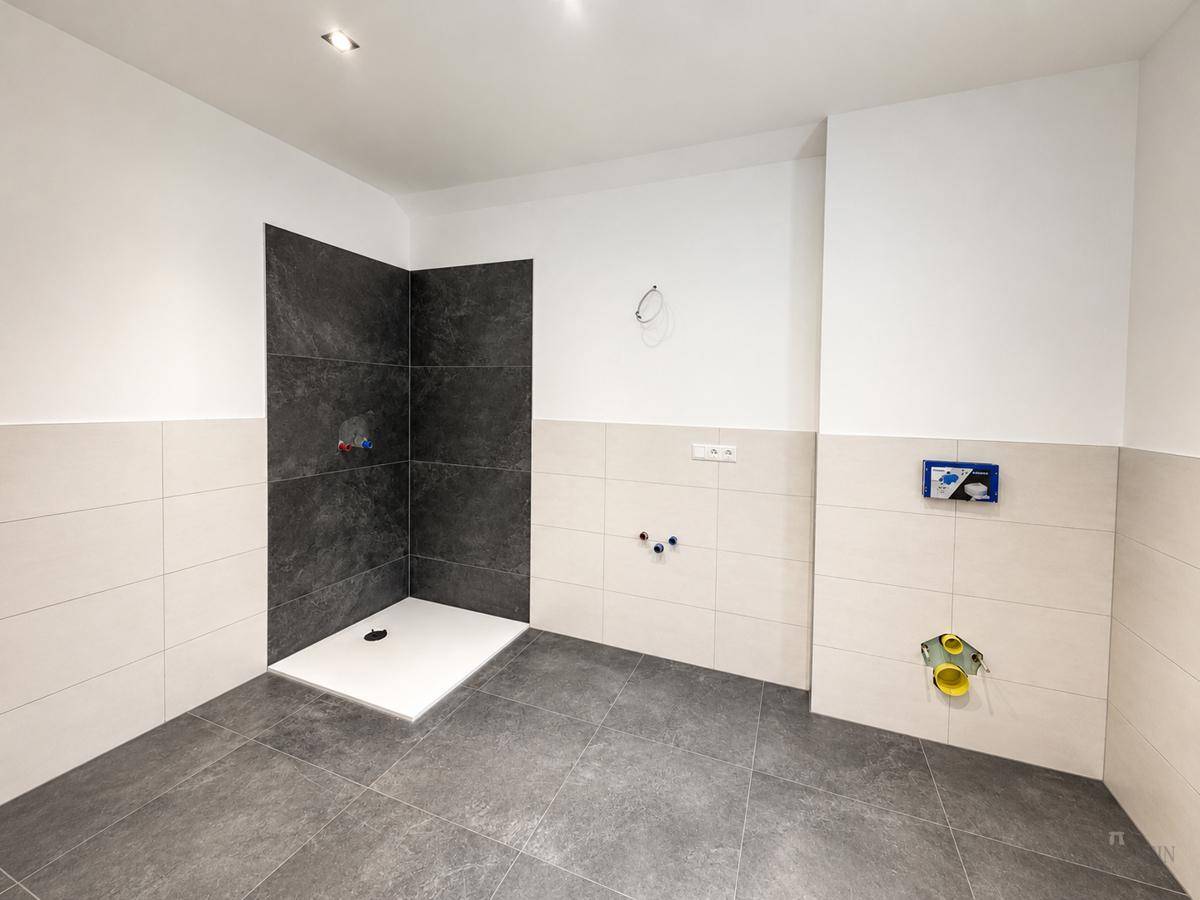 Unfertiges Badezimmer mit modernen Fliesen und vorbereitetem Duschbereich, bereit für die Endmontage der Sanitärobjekte.