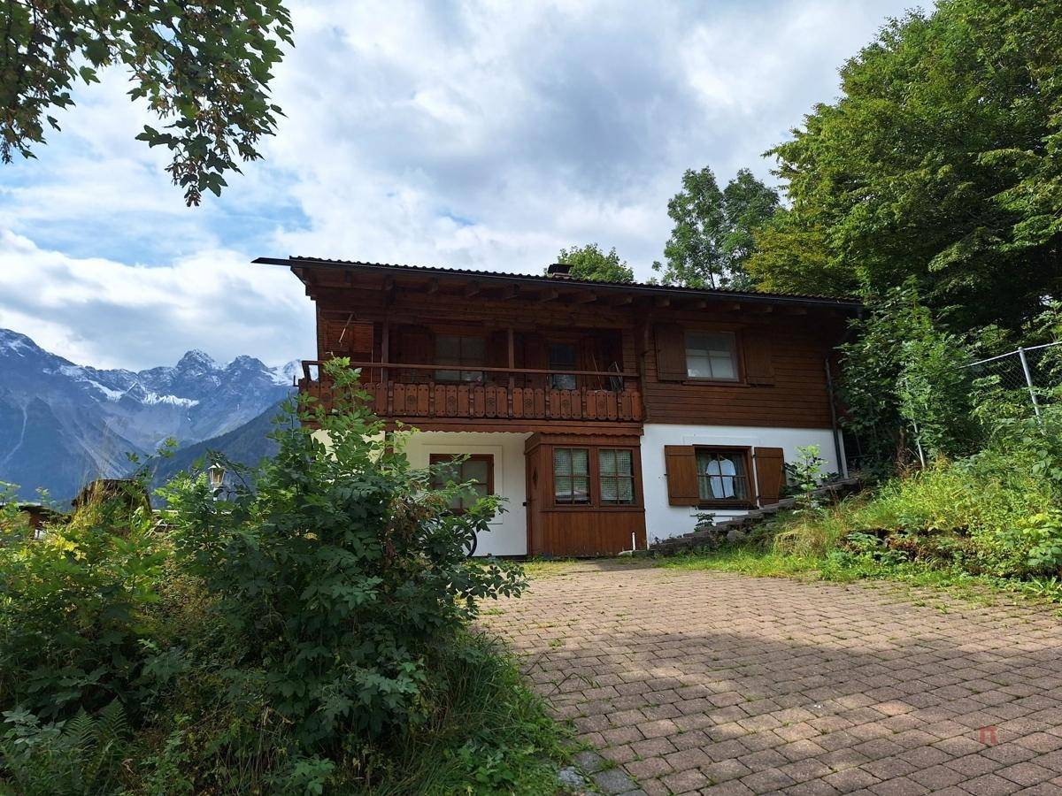 Traditionelles Holzhaus im Chalet-Stil mit gepflasterter Auffahrt und Bergblick im Hintergrund.