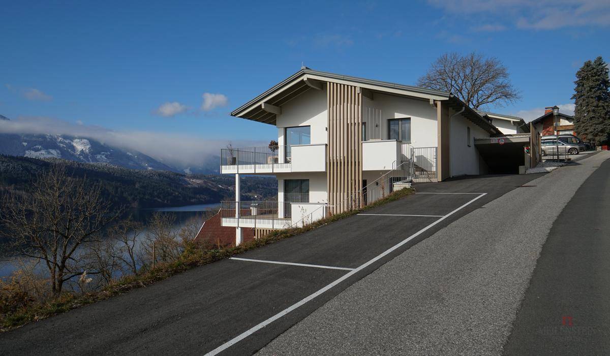 Modernes Haus am Hang mit Balkonen, Seeblick und Bergblick, umgeben von Natur.