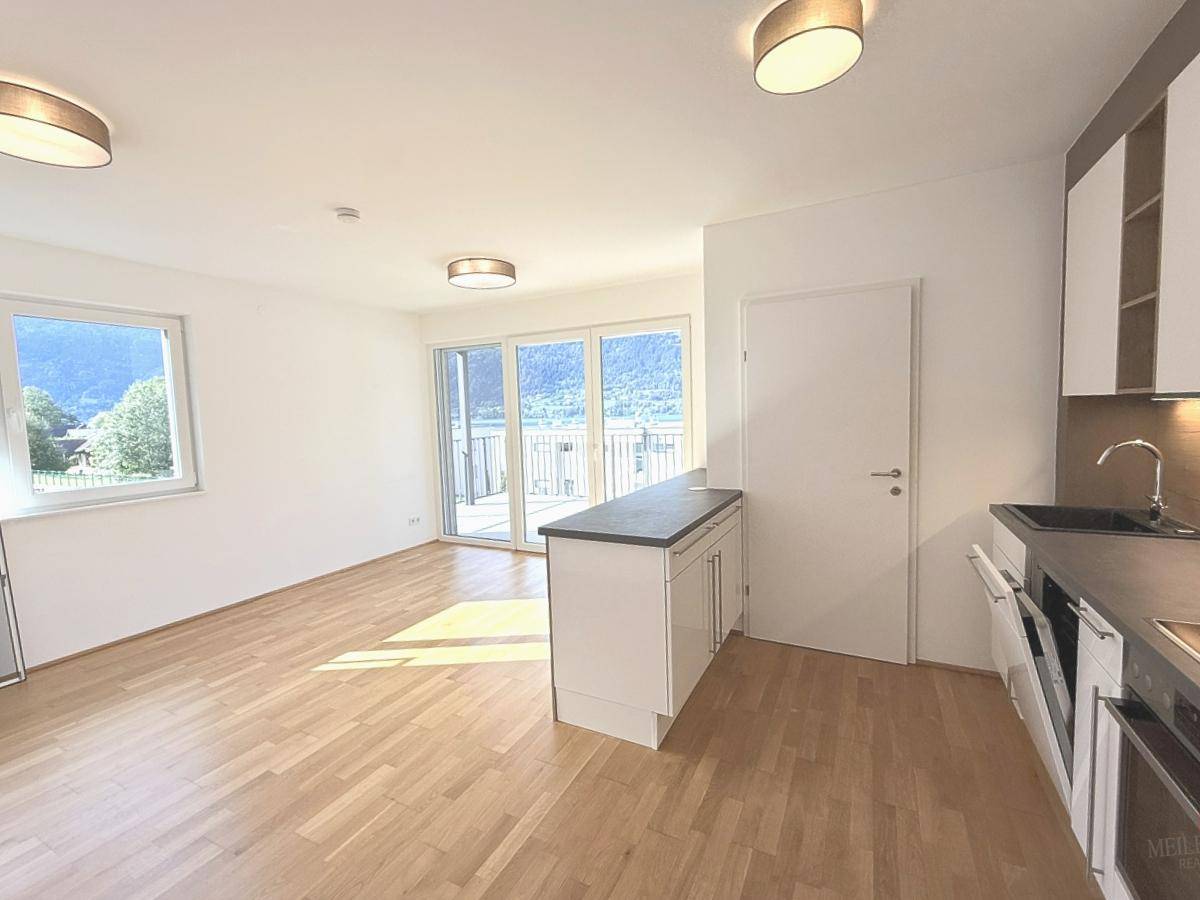 Lichtdurchfluteter Wohnbereich mit offener Küche, Parkettboden und großem Fenster mit Bergblick.