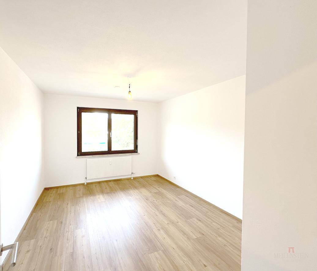 Helles Zimmer mit Holzfußboden und weiß gestrichenen Wänden, ideal als Schlafzimmer.