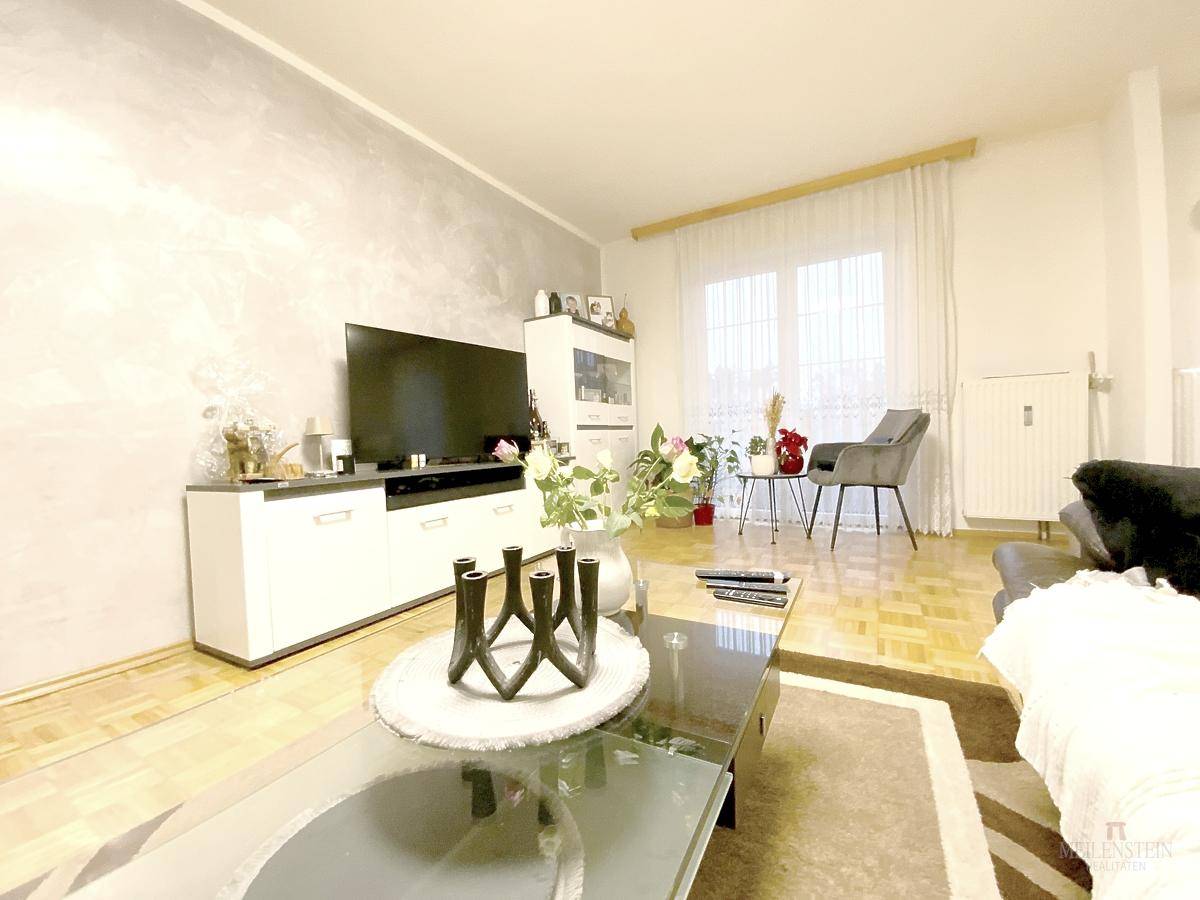 Gemütliches Wohnzimmer mit Parkettboden, modernem TV-Möbel und hellem Fensterbereich.
