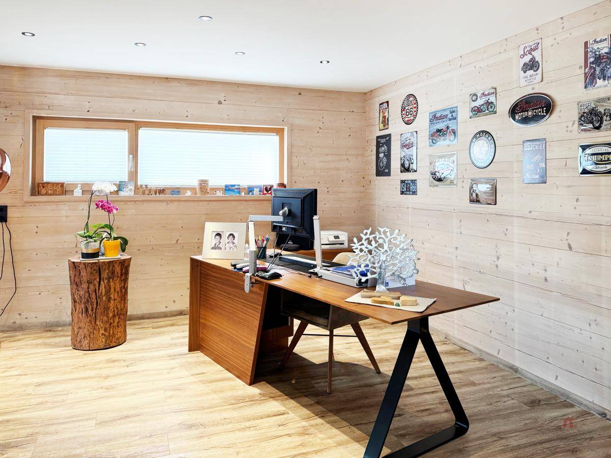Helles Arbeitszimmer mit Holzwänden, großem Schreibtisch und dekorativen Postern an der Wand.