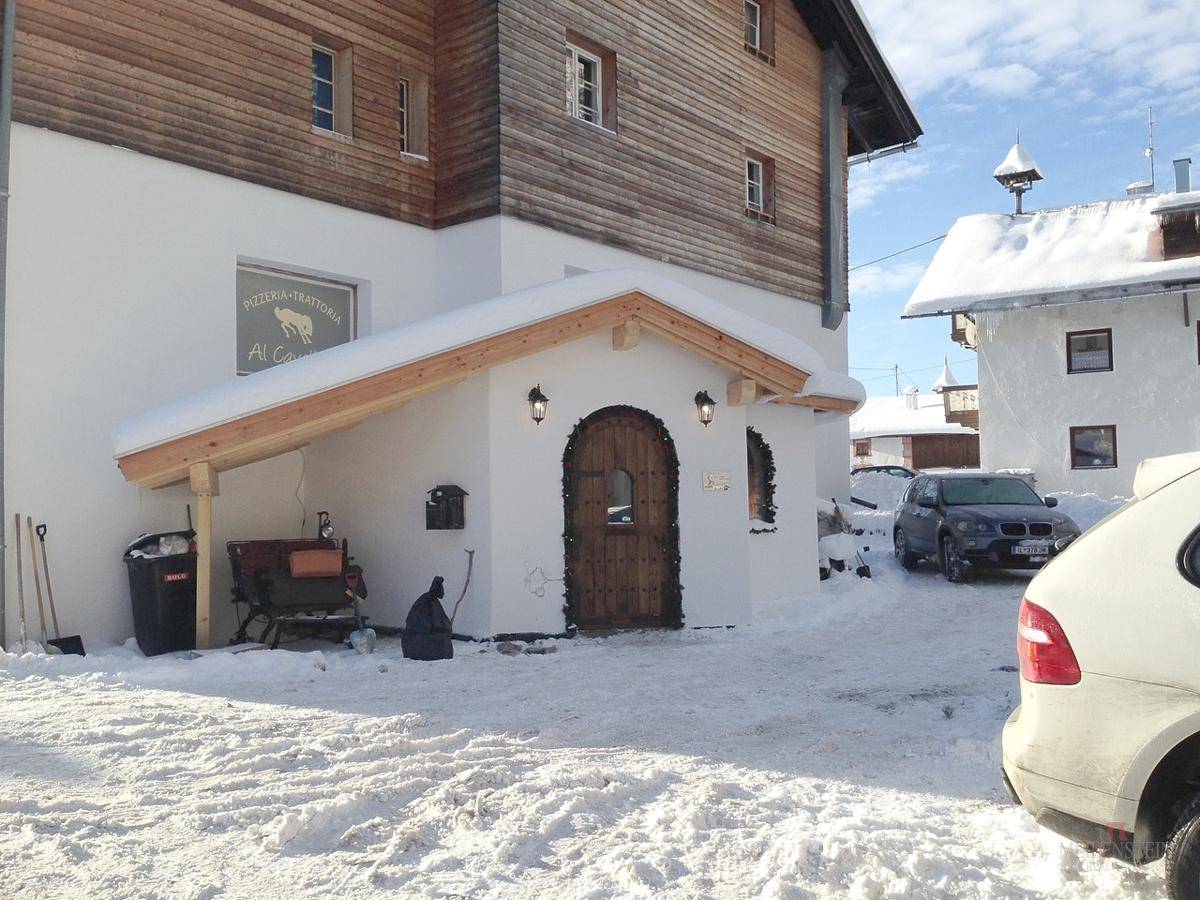 Rustikaler Eingangsbereich eines Gebäudes mit Holztür und Schnee auf dem Vordach.
