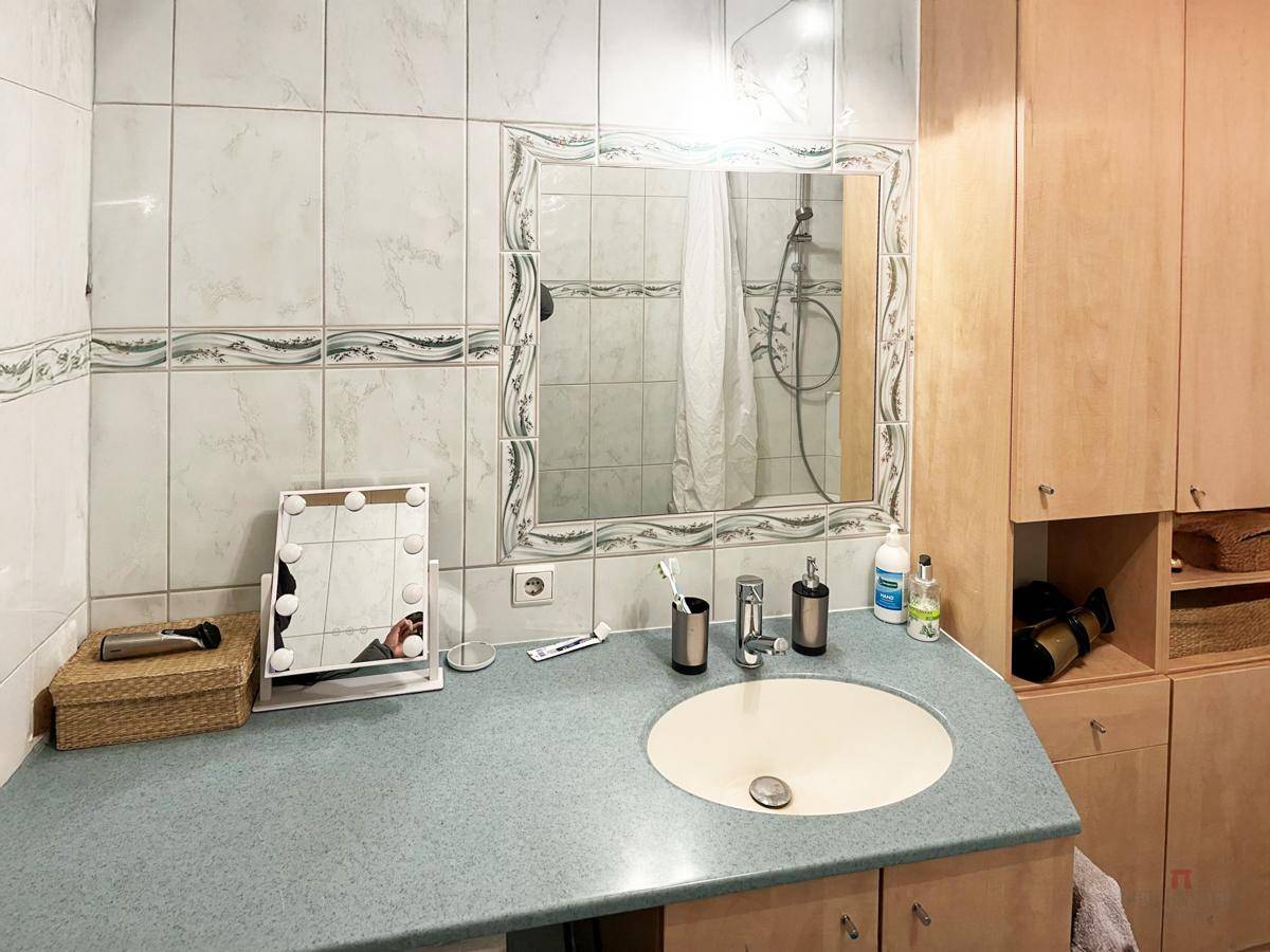 Badezimmer mit Einzelwaschbecken, großem Spiegel und Holzschränken für Stauraum.
