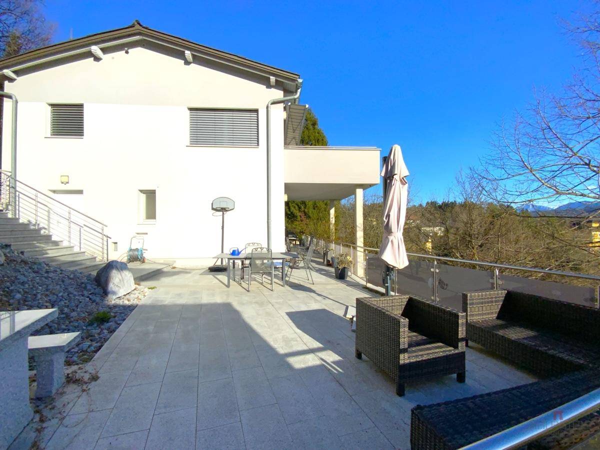 Weitläufige Terrasse mit modernen Loungemöbeln, Esstisch und Glasgeländer unter blauem Himmel.