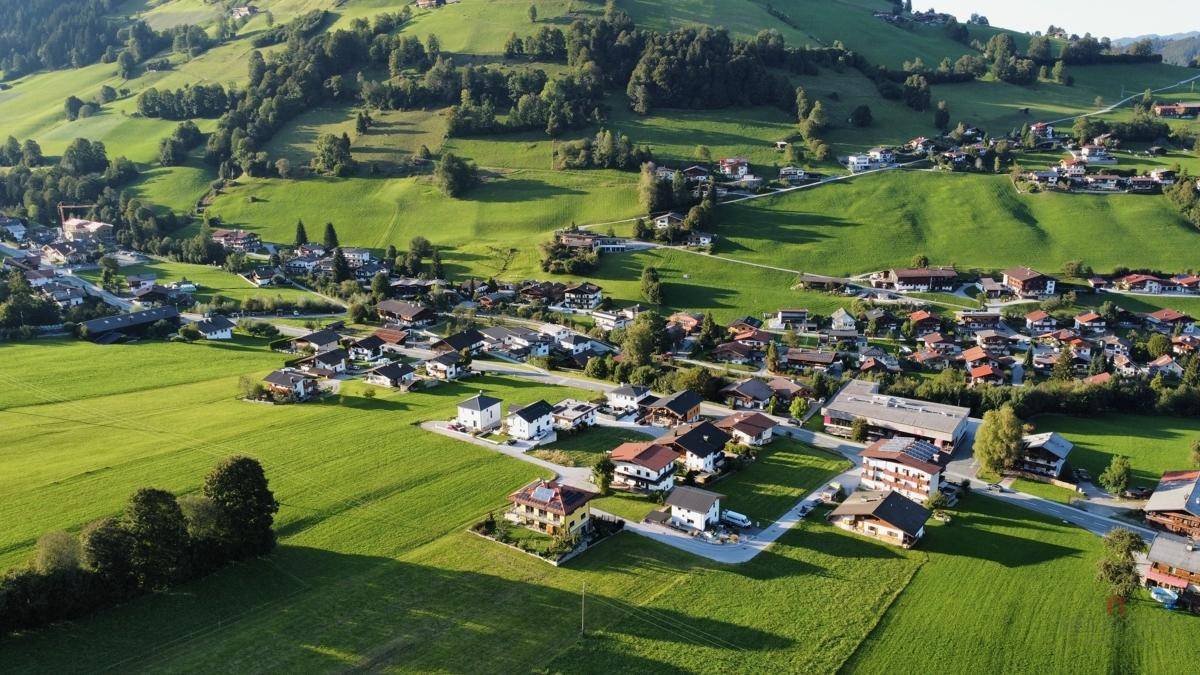 Weitläufige Luftaufnahme einer Siedlung eingebettet in eine idyllische grüne Berglandschaft.