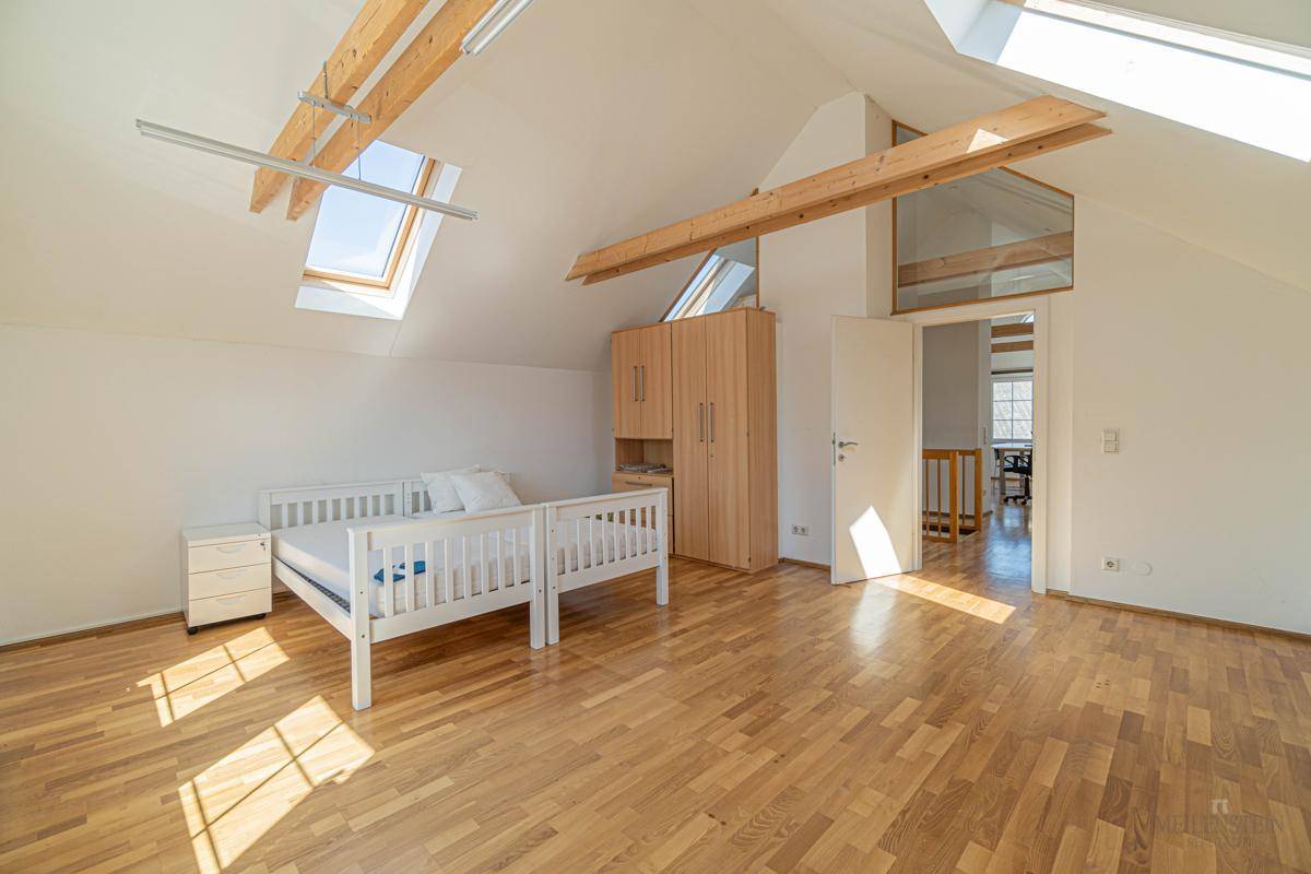 Geräumiges Dachgeschoss-Schlafzimmer mit Holzboden, Dachfenstern und einem Kleiderschrank.