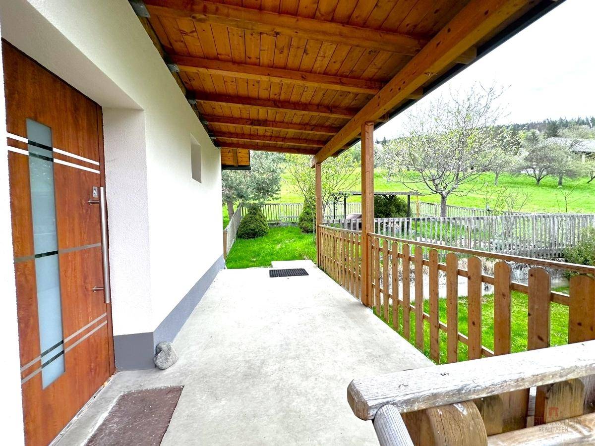 Überdachte Holzveranda mit rustikalem Geländer und weitem Blick in die grüne Landschaft.