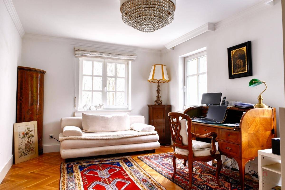 Helles Arbeitszimmer mit Parkettboden, Schreibtisch und bequemer Couch.