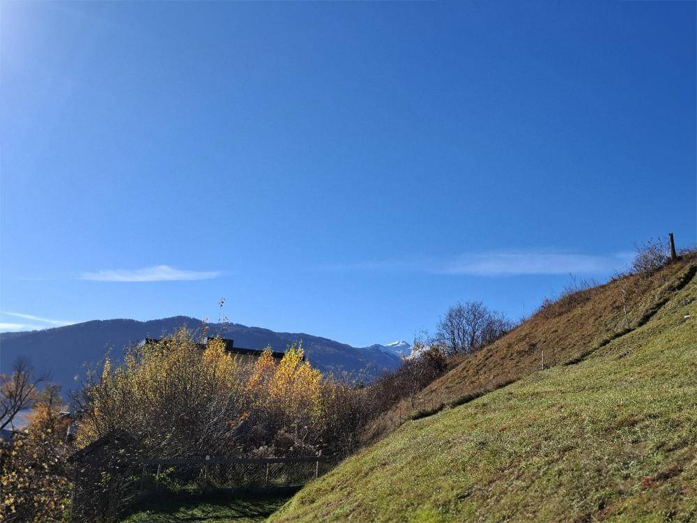 Weitläufige Berglandschaft unter blauem Himmel mit grünen Hängen und einem Gebäude im Tal.