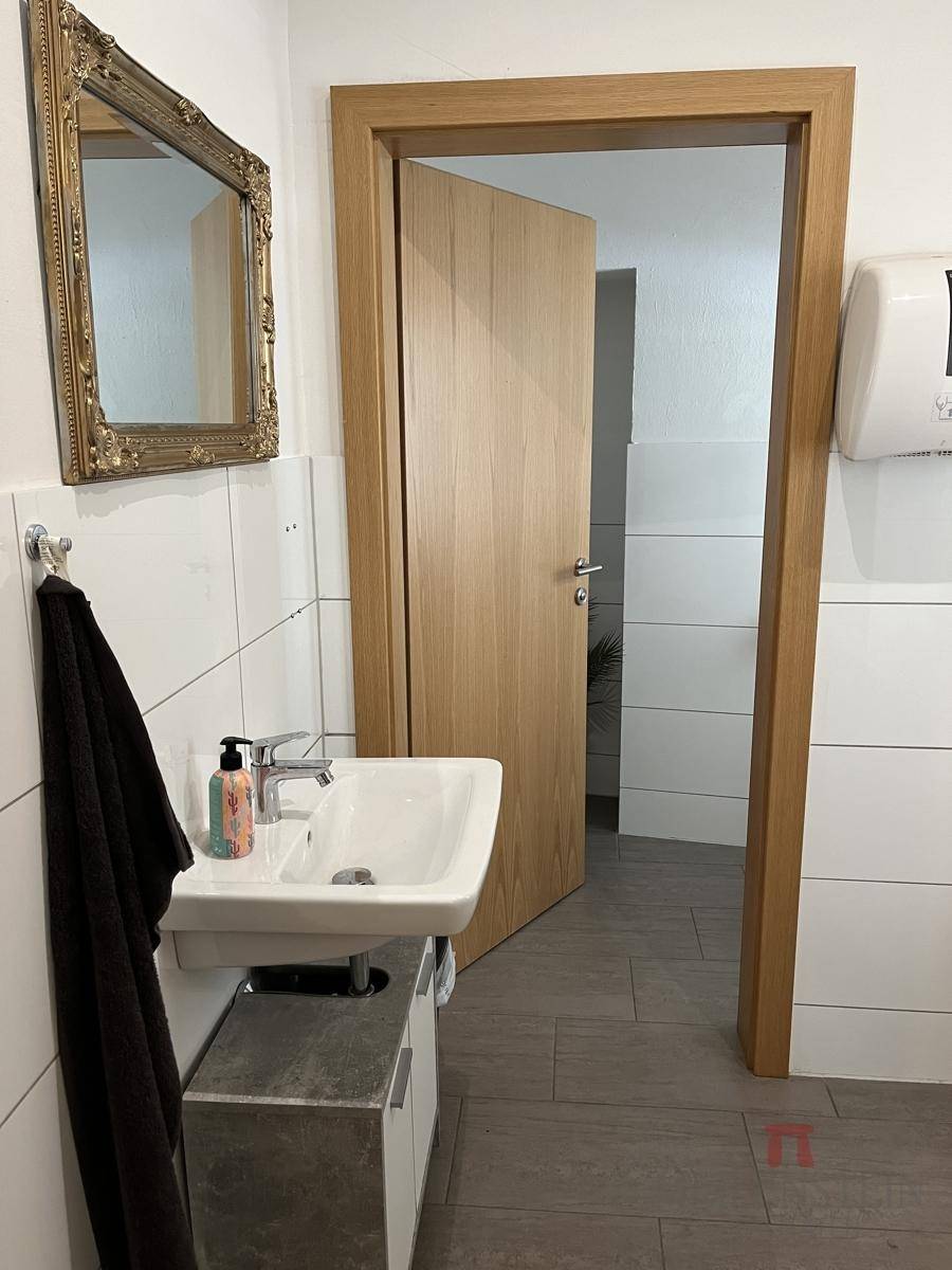 Badezimmer mit einem Waschbecken, weißen Fliesen und einem verzierten goldenen Spiegel.