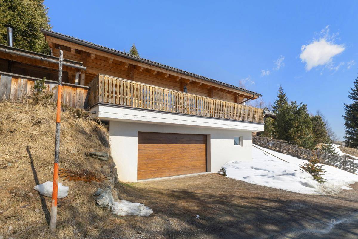 Ansicht des Holzchalets mit integrierter Garage und Balkon im Winter.