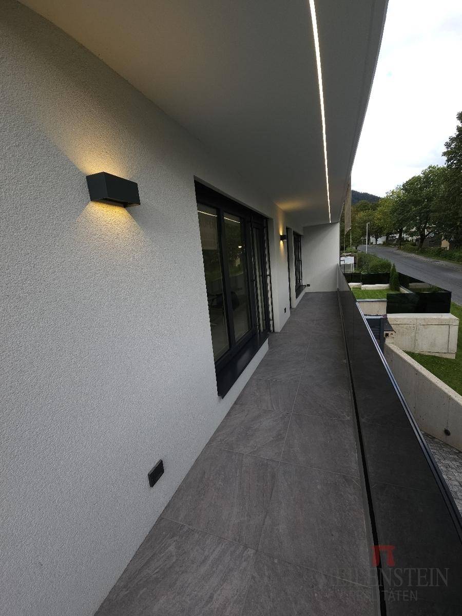 Langer, überdachter Balkon mit Fliesenboden und integrierter Deckenbeleuchtung.