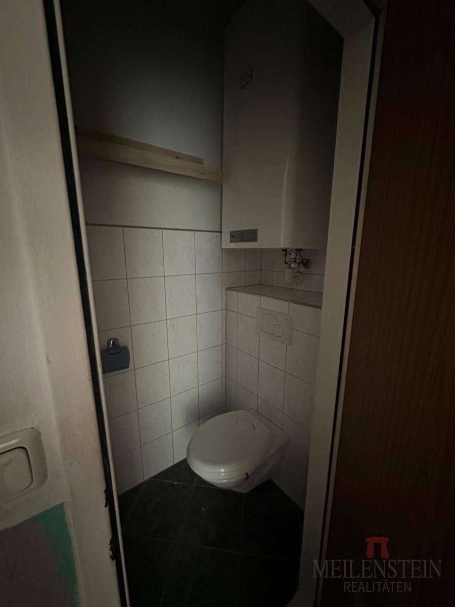 Kleines WC mit Toilette und wandmontiertem Boiler in einem dunklen Raum.