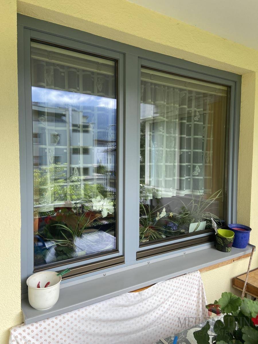 Fenster mit Blick auf die umliegenden Gebäude und Pflanzen, das viel Tageslicht hereinlässt und eine helle Atmosphäre schafft.
