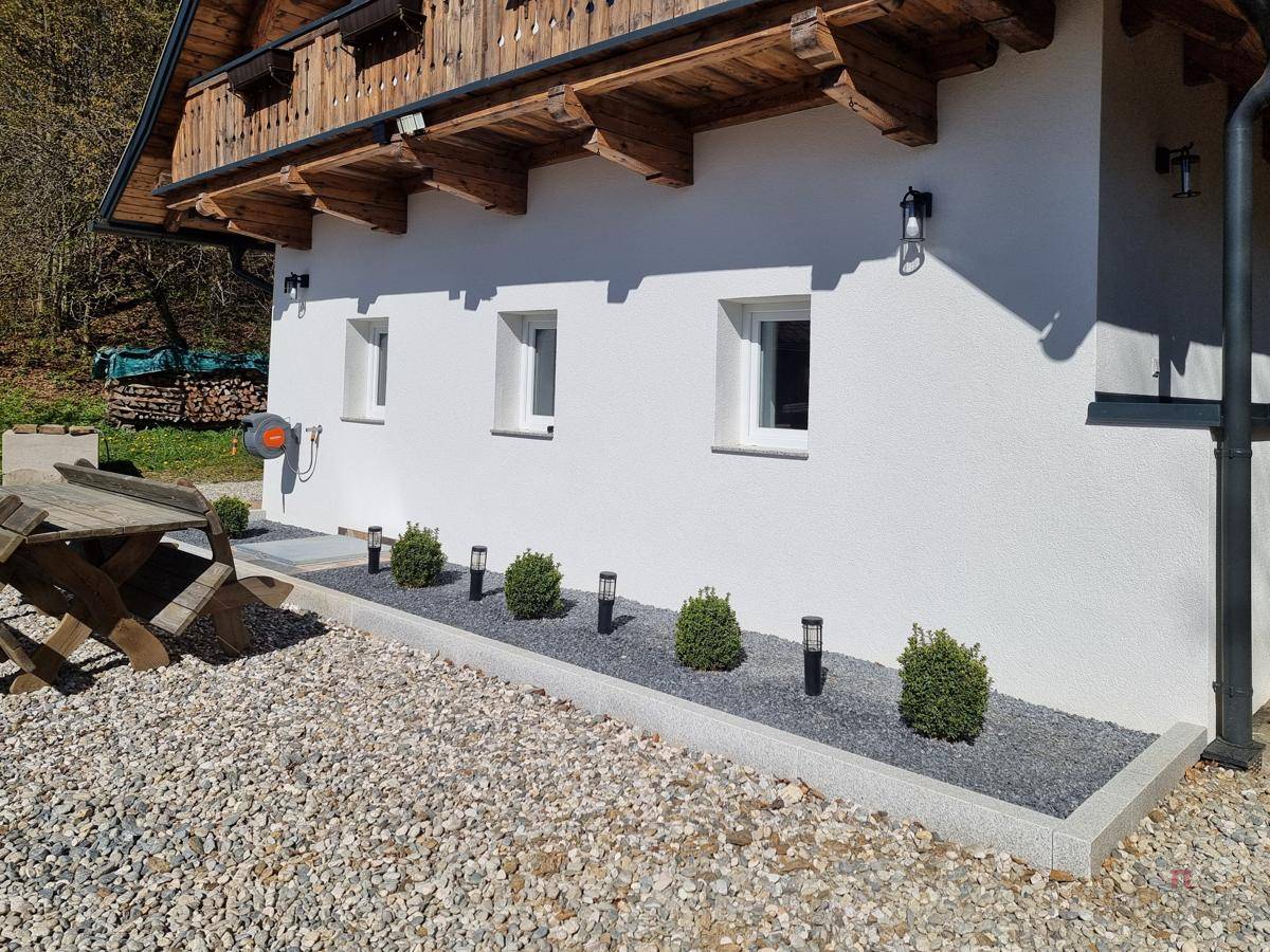Detailansicht der Hausfassade mit kleinen Fenstern, dekorativen Sträuchern und Kiesbeet.