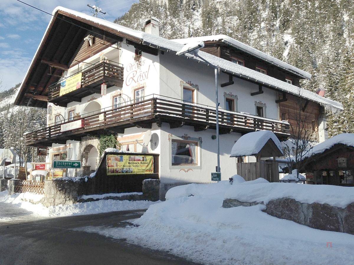 Traditionelles Gasthaus mit Holzbalkonen und verschneiter Umgebung vor Bergkulisse.