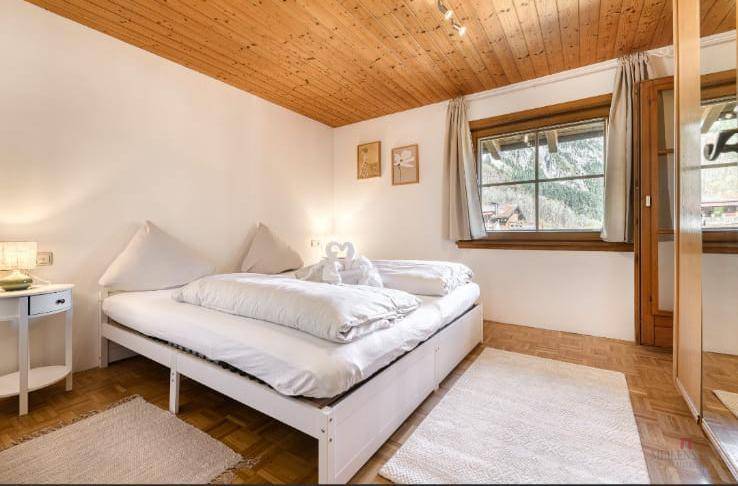 Helles Schlafzimmer mit Holzbalkendecke, Doppelbett und Blick auf die umliegende Natur.