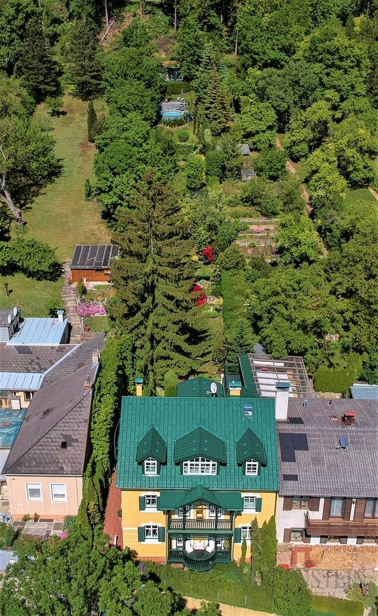 Luftaufnahme eines charmanten gelben Hauses mit grünem Mansarddach, umgeben von üppigem Grün und einem weitläufigen Garten mit Pool.