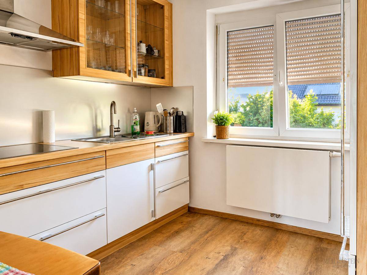 Helle Küche mit Holz- und weißen Fronten, Induktionskochfeld und Fenster mit Rollladen.