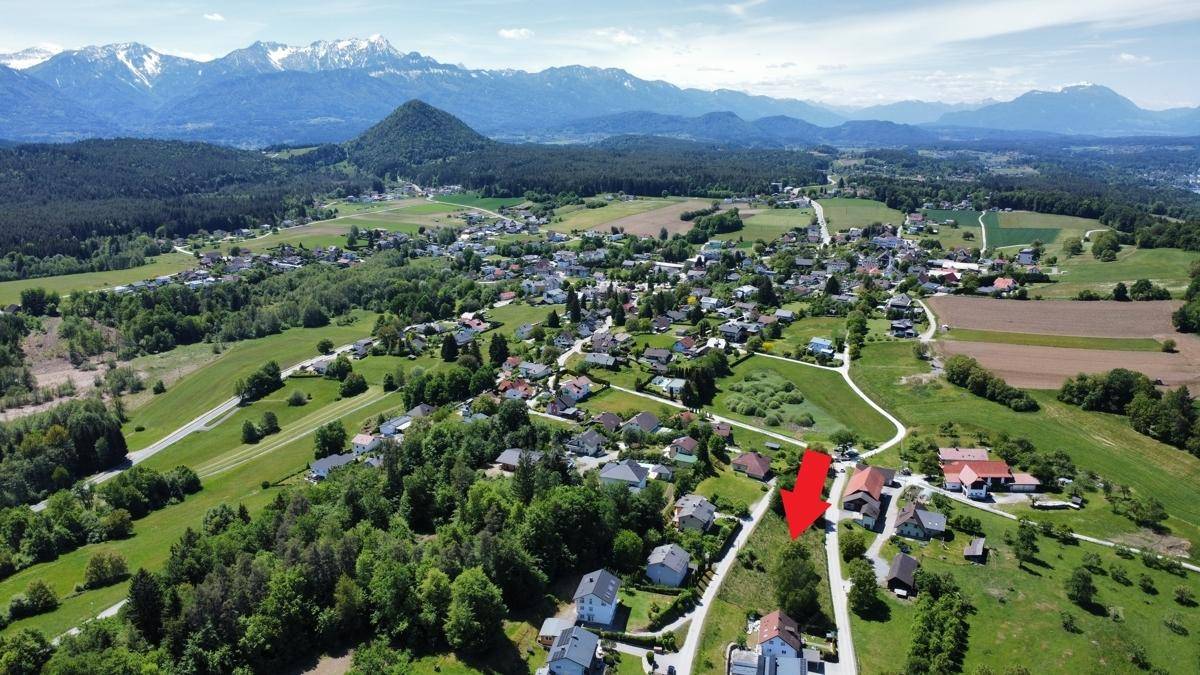 Luftaufnahme einer ländlichen Gegend mit Häusern und Bergen im Hintergrund, das Grundstück ist mit Pfeilen gekennzeichnet.