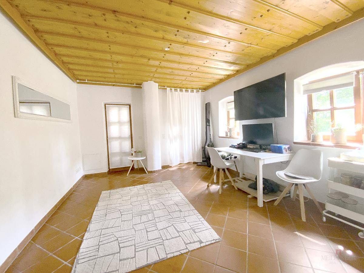 Geräumiges Zimmer mit Holzbalkendecke, Fliesenboden und Arbeitsplatz am Fenster.
