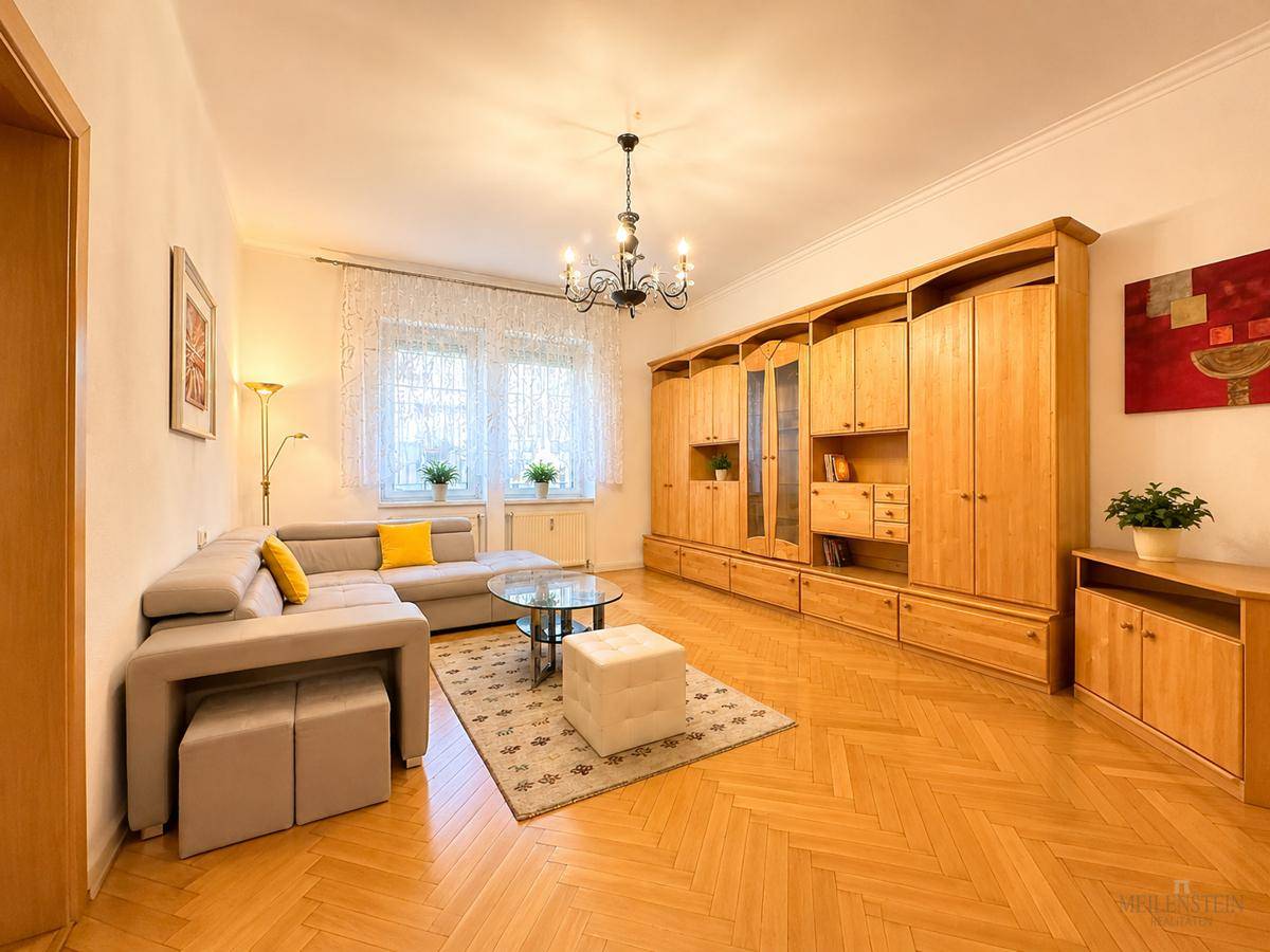 Geräumiges Wohnzimmer mit Fischgrätparkett, großer Holzschrankwand und bequemer Sitzecke.
