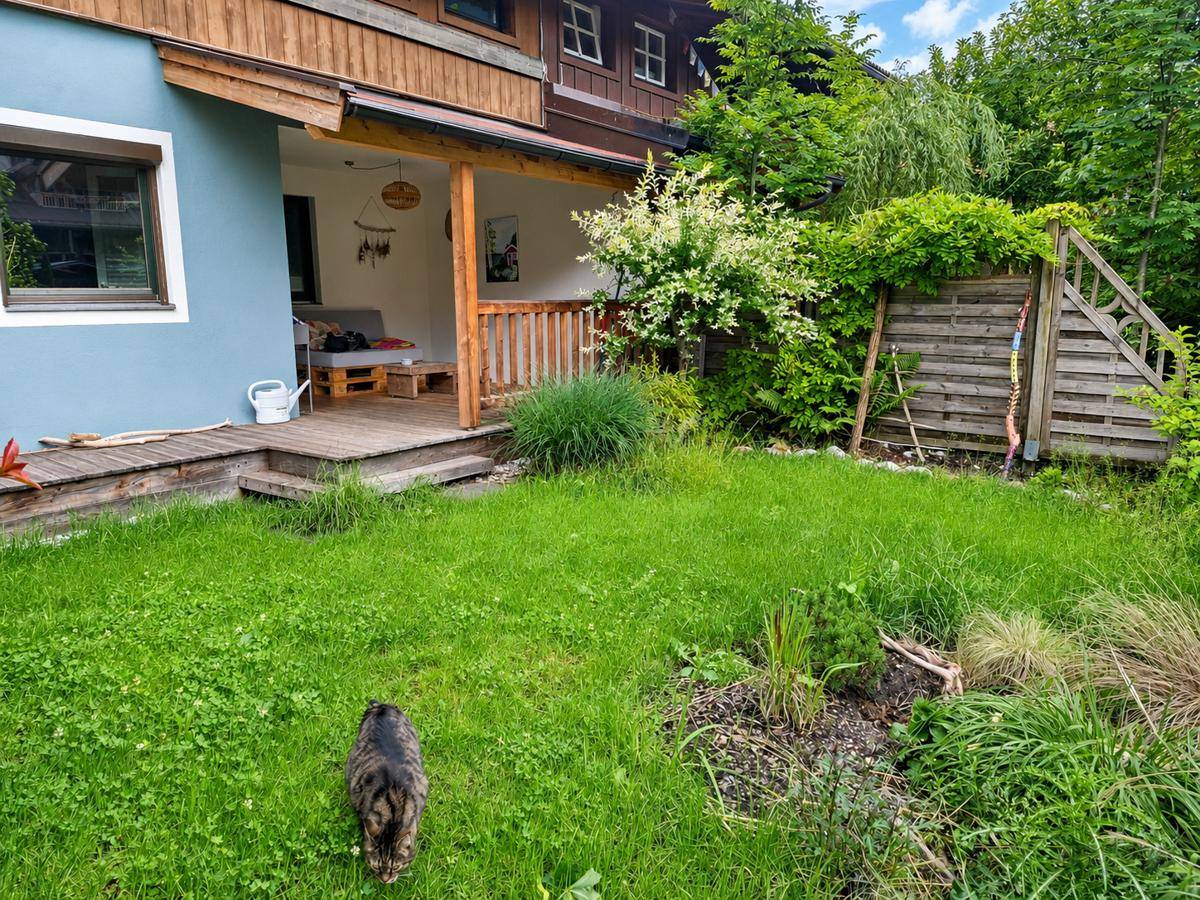 Gartenbereich neben dem Haus mit Rasen, Pflanzen und Zugang zum überdachten Außenbereich.